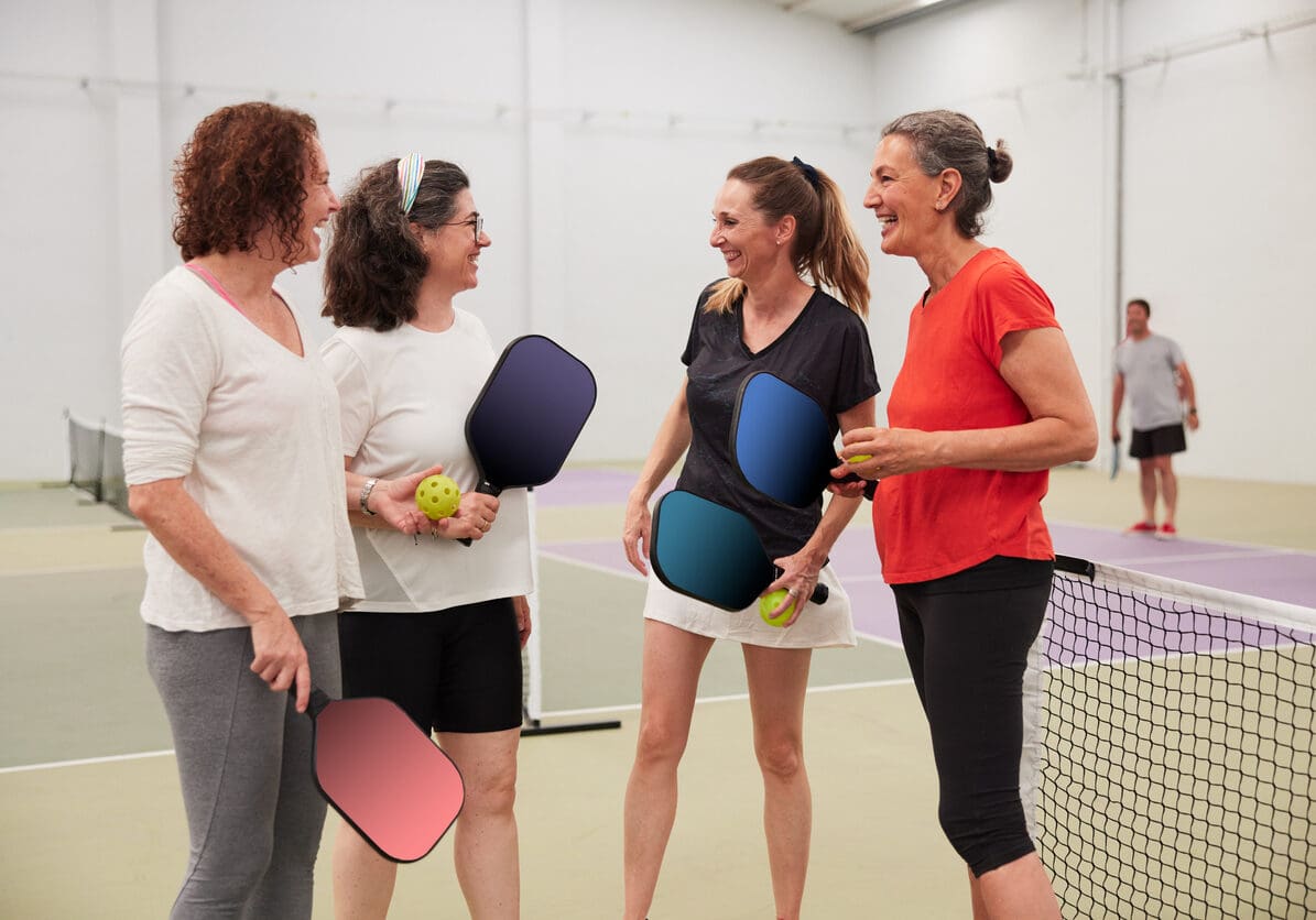 Four middle-aged women stand next to the net in sports attire.