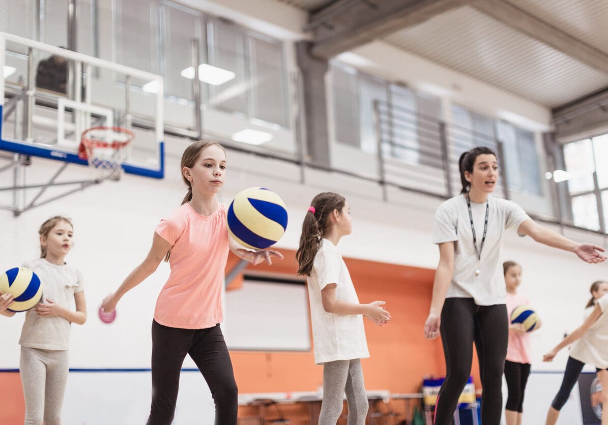 Female coach talking with girls at volleyball court. She teaching them  how to play better